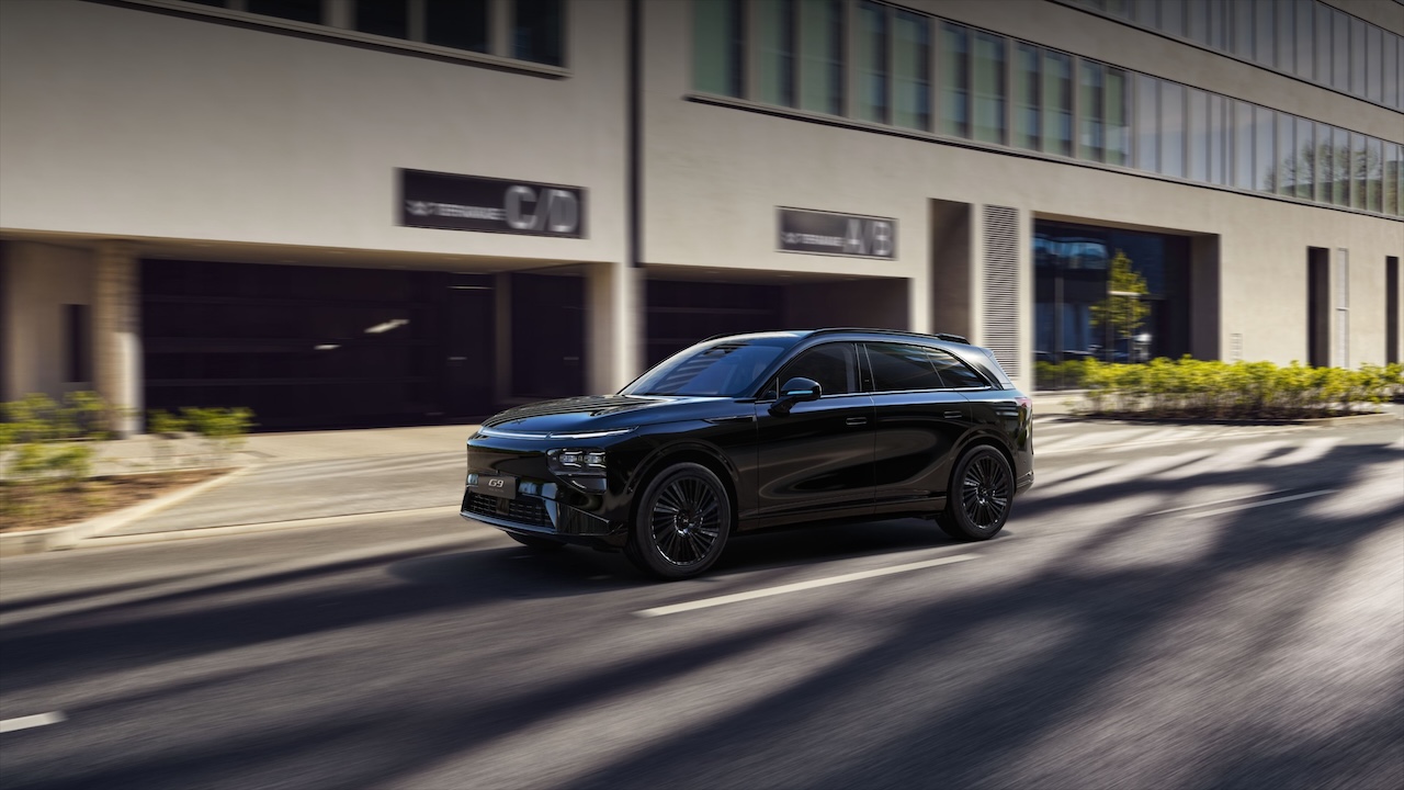 Ein schwarzes SUV fährt auf einer städtischen Straße an einem modernen Gebäude vorbei